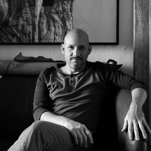 Man sitting on a couch in a room with books and artwork.