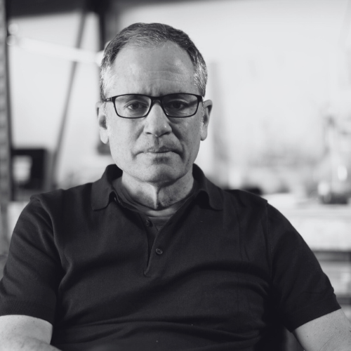 Black and white portrait of a man wearing glasses and a dark shirt.