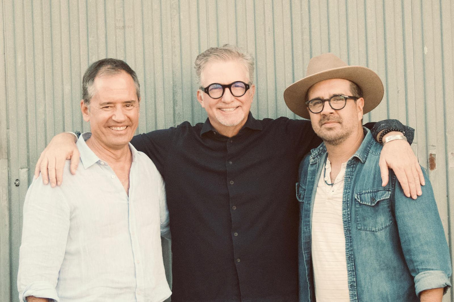 Three men standing together with arms around each other against a plain background