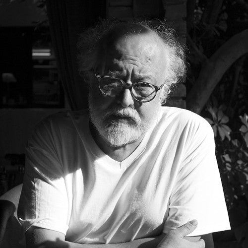 Black and white photo of a man with glasses and a beard sitting outdoors.