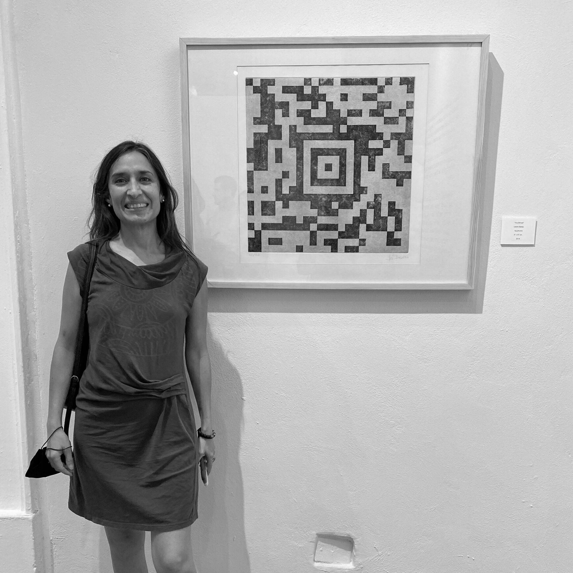 Woman standing in front of a framed black and white abstract artwork on a wall.